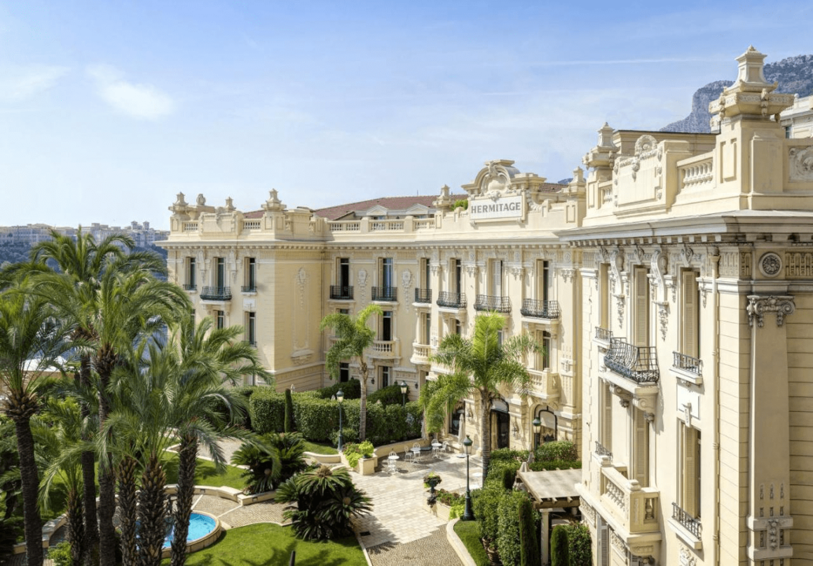 "Majestueus hotel in Monaco, omgeven door een prachtig aangelegde tuin vol exotische planten en bloemen."