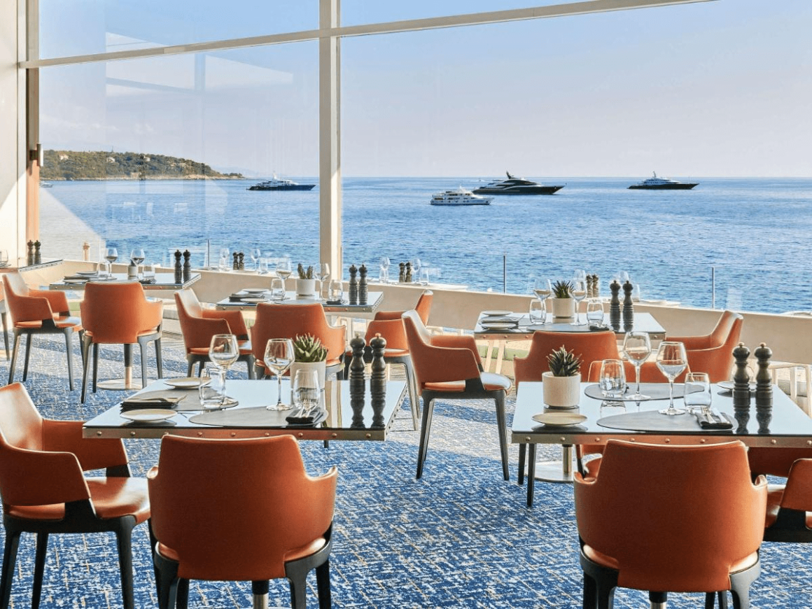 Betoverend uitzicht vanuit een restaurant in Monaco, met een panoramisch zicht op de luxueuze jachten die op de sprankelende Middellandse Zee dobberen.