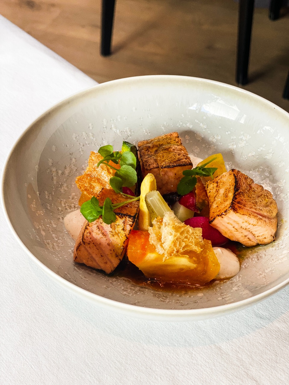 An artistically presented dish of marinated and grilled wild salmon, accompanied by fresh tomato, avocado and radishes, served on a modern plate at De Bakermat restaurant.