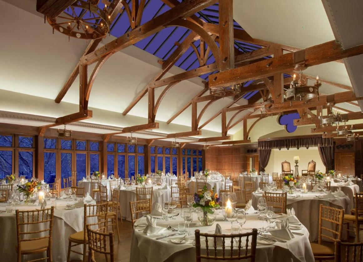 De eetkamer van Crossbasket Castle, gekenmerkt door zijn elegantie en grandeur. De kamer is prachtig verlicht met een grote kristallen kroonluchter, waardoor de goed gedekte eettafels en pluchen stoelen een gedenkwaardige eetervaring bieden.