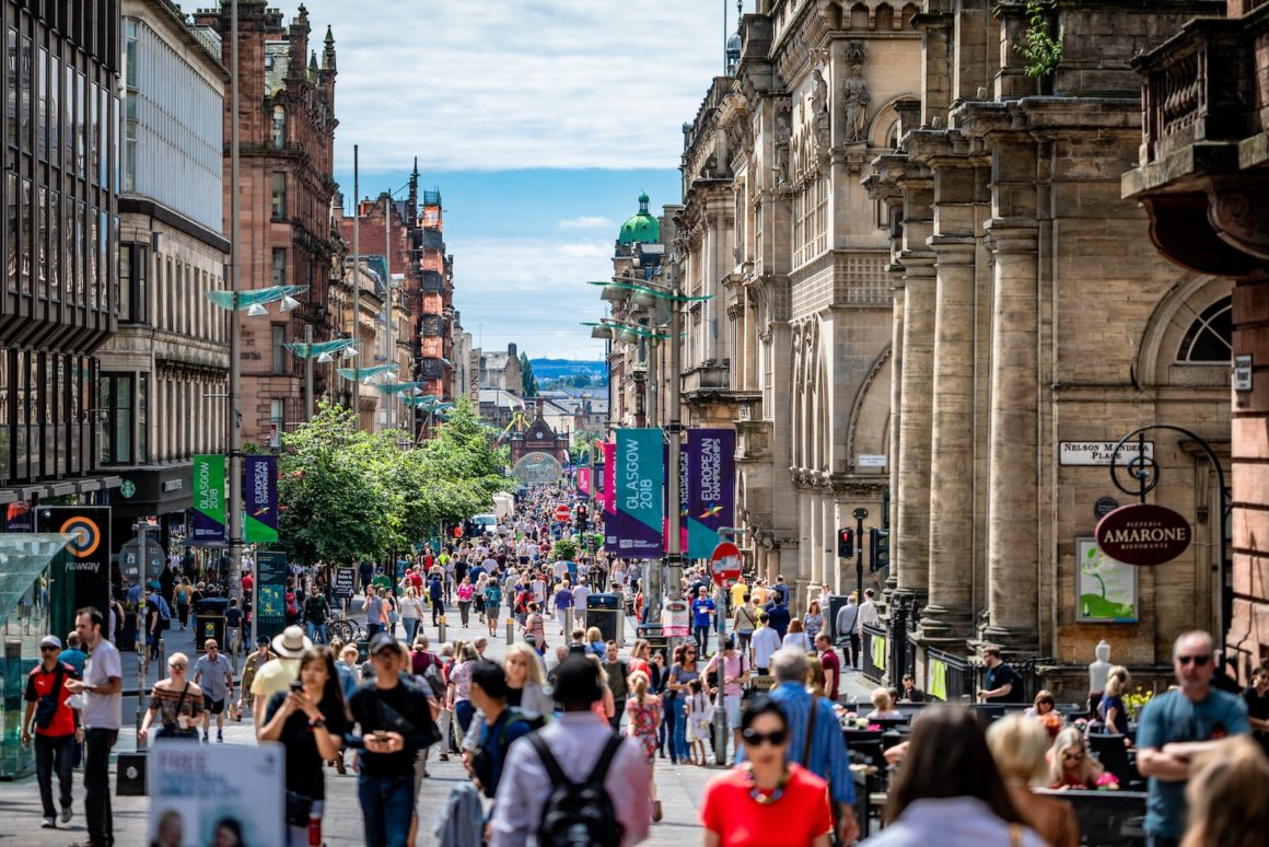 A lively panorama of Glasgow, showcasing the city's blend of historic architecture and modern cityscape, bustling with energy amid the backdrop of the lush Scottish landscape.