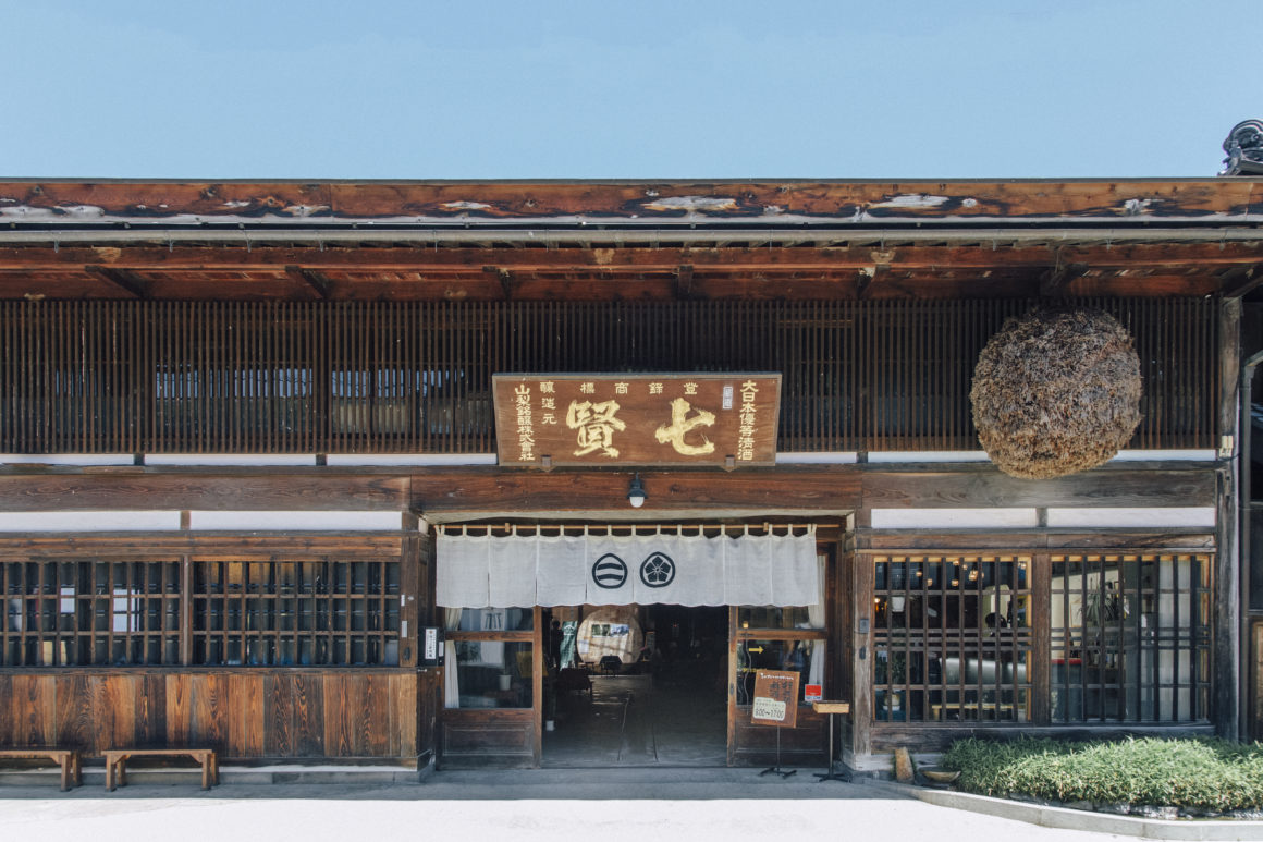 Shichiken Brewery exterieur: traditioneel Japans gebouw omringd door sakévaten en groene landschapsarchitectuur.