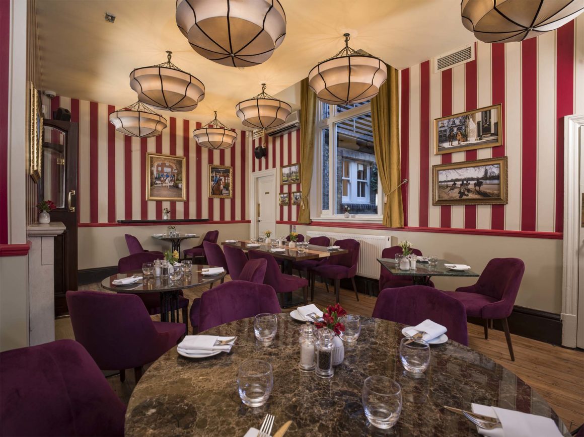 Interieur van The Stablehand restaurant in Londen met rode en witte gestreepte muren, hangende lantaarnlampen, paarse fluwelen stoelen en historische foto's aan de muur