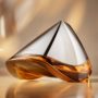Close-up of the futuristic Bowmore ARC-54 whisky decanter, designed in collaboration with Aston Martin. The hand-blown vessel features a sleek silver top and amber-colored whisky below, set against a warm, golden-toned background. On the left are the Aston Martin and Bowmore logos; on the right, the text reads “ARC-54 from Bowmore