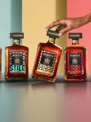 The five Disaronno 500-year limited edition bottles displayed in a vibrant setting, with a hand gently touching the Dolce Vita bottle.