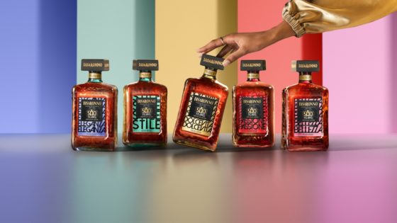The five Disaronno 500-year limited edition bottles displayed in a vibrant setting, with a hand gently touching the Dolce Vita bottle.