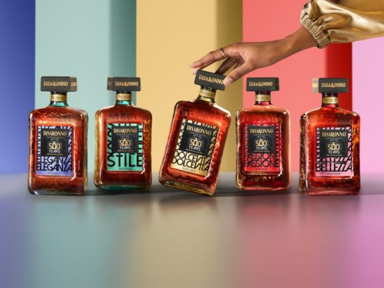 The five Disaronno 500-year limited edition bottles displayed in a vibrant setting, with a hand gently touching the Dolce Vita bottle.